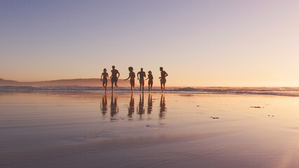 Group Of Friends In Swimwear Run Out Of Waves At Sunset On Summer Beach Vacation