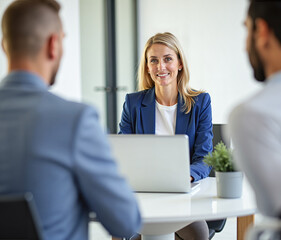Female consultant or bank employee in her thirties sitting at a desk behind her laptop computer consulting two male  clients - or small team meeting