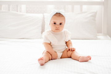 Cute newborn baby girl sitting on a bed in white clothes in a br