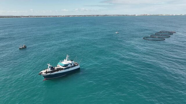 A Mid sized marine vessel tows four fish farms along the west Australian coast.