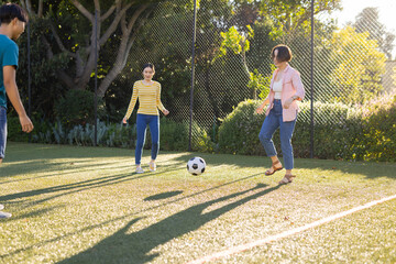 Playing soccer on field, asian family enjoying outdoor activity together in park