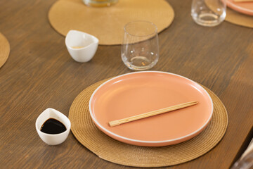 Chopsticks on pink plate with soy sauce and glass on dining table
