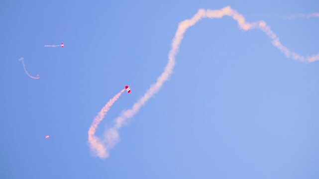 British Red Devils military parachute team performs a high-speed aerial descent with red smoke trails. The display captures skydivers in freefall, leaving dramatic smoke patterns in the sky.