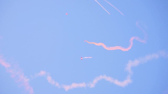 British Red Devils perform an intricate parachute display, leaving winding smoke trails in the clear sky. The image captures precise aerial maneuvers during a military parachuting event