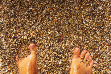 A persons foot is resting gently on the warm sand at the beach