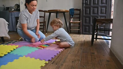 Mother and toddler playing together on colorful mats at home with a xylophone, fostering early childhood development through music and bonding.