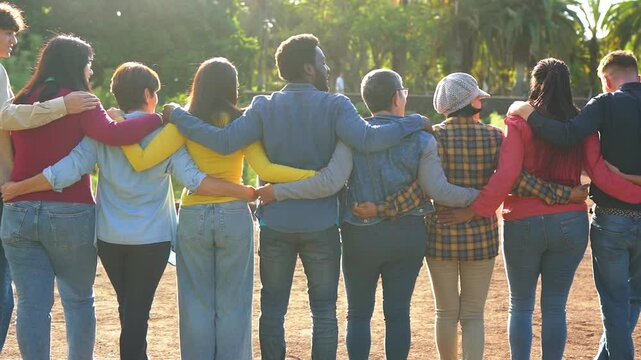 Group of multi generational people having fun hugging each other outdoor - Crowd of multiracial friends enjoy day at city park - Concept of humanity and community