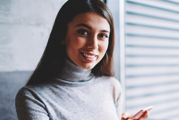 Portrait of successful carefree female blogger using smartphonefor making transaction in web store...