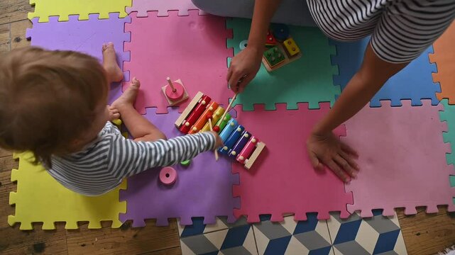 Top view of a child playing with colorful toys on a foam mat with adult assistance, promoting learning and development