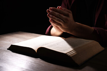 Man with Bible praying at wooden table, closeup