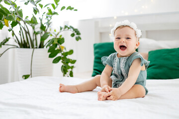 little baby girl on the bed at home in a green bodysuit smiling or laughing, cute funny baby at...