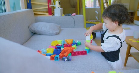 A young child girl engaged in creative play with vibrant building blocks in a sunlit living room, fostering imagination and development.