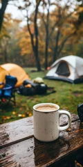 Gordijnen A ceramic coffee mug on a wet picnic table, with a camping setup in the background on a rainy winter day. © David Zarzosa