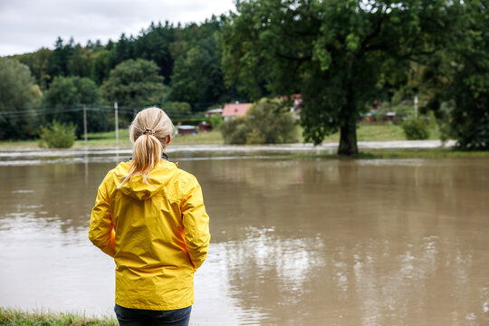 Flooded river. Worried woman looking at overflowing water during flood. Extreme weather and natural disaster due to climate change