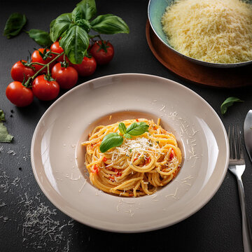 Fotografia gastron&ocirc;mica macarronada cremosa. Queijo ralado,  manjeric&atilde;o, um prato de tomate fresco &agrave; esquerda e ervas &agrave; direita.  Tomada de &acirc;ngulo alto inspirado em fotografia editorial.