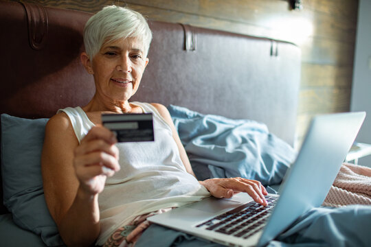 Senior woman shopping online with credit card in bed