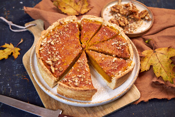 Homemade pumpkin spice pie for the Thanksgiving holiday. Top view with dark background with maple leaves