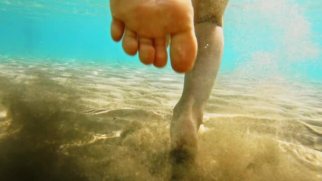 close up with bare feet of a child in the water swimming and running lifting the sand from the bottom of the sea. Child bare foot in the water. Baby swims with inflatable coil - underwater view.