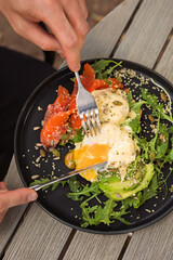 Man eating eggs Benedict with Hollandaise Sauce on toasted bread with avocado, arugula and salmon