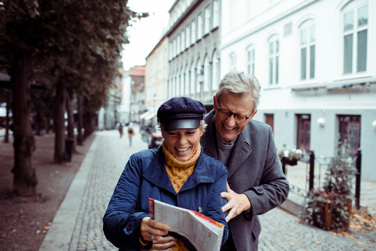 Senior couple laughing and exploring city with a map - Powered by Adobe