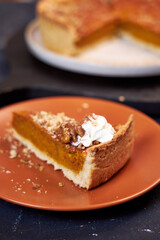 pumpkin pie on a dark background on a terra cotta plate. Top view