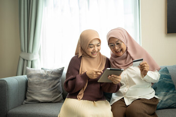 Happy muslim mother and daughter shopping online with digital tablet in a living room