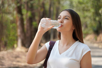 Portrait of young woman drinking water from plastic bottle. Brazilian Caucasian girl drinking water in the park.