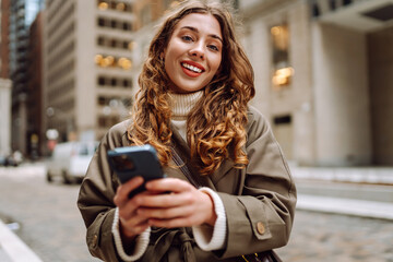 Attractive woman in trench coat using phone outdoor in the street. Lifestyle, travel, tourism, technology