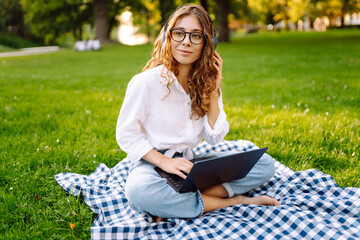 Portrait of attractive young woman sitting on green grass in park with legs crossed during summer...