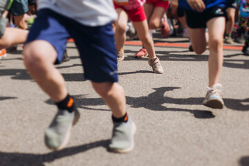 Fototapeta premium Children marathon runners crowd, young teen sportsmen participants start running in the city streets, crowd of kids joggers in motion, kid group athletes outdoor run, family competition in summer day