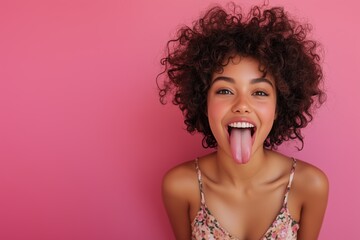 Close up studio portrait of young mixed race woman with curly hairstyle isolated on pink background showing tongue and laughing