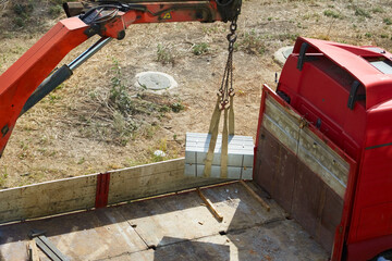loader crane unloads concrete garden barriers from the truck bed, construction work with curb stones