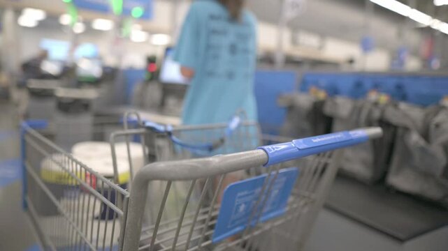 Close-up of a shopping cart in a supermarket self-checkout area, with a customer in the background. High quality 4k footage