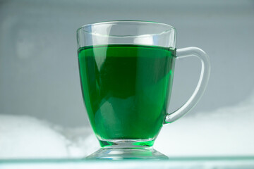 glass cup with green liquid inside which is green. frozen ice snow background in freezer
