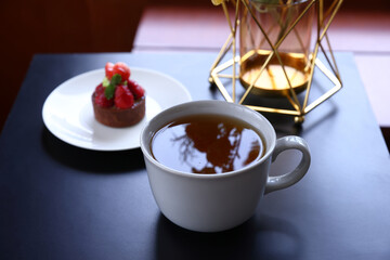 A cup of hot tea with black background, wood background, with a cup of hot tea in hand ,warm photo.