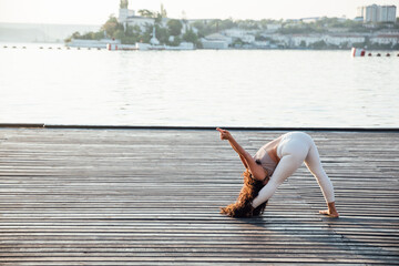 Pretty healthy woman doing active training exercise on a yoga mat near the ocean. Coastal yoga tranquility
