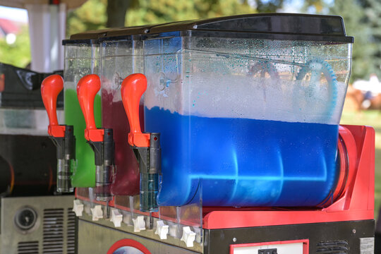 Slush machine making colorful frozen drinks with different flavors, refreshing beverages with ice in blue, red and green at a funfair market