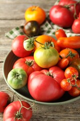 Different ripe tomatoes in bowl on wooden table, closeup