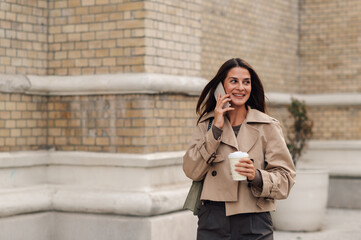 Stylish businesswoman walking and talking on phone with coffee