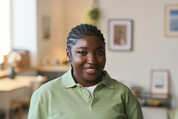 Front view portrait of young Black woman wearing uniform standing in home interior and smiling at camera, copy space