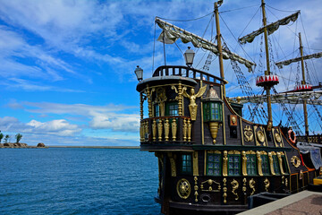 drewniany statek turystyczny ze złotymi dekoracjami, stylizowany piracki statek turystyczny stojący w porcie, wooden tourist ship with golden decorations, golden ancient ship standing in the port © kateej