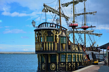 drewniany statek turystyczny ze złotymi dekoracjami, stylizowany piracki statek turystyczny stojący w porcie, wooden tourist ship with golden decorations, golden ancient ship standing in the port © kateej