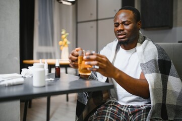 African American man sick with flu or cold at home. He takes medicine and drinks tea