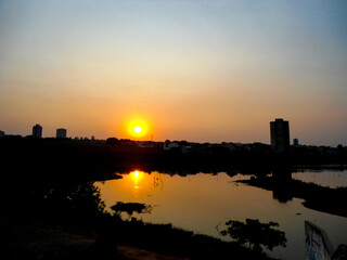Fototapeta premium Peaceful evening at the lake, watching the sun dip below the horizon. The city lights begin to twinkle, creating a magical ambiance.