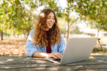 Young woman brought her laptop to the park to get some fresh air and work. Online education, Freelance work, technology concept.