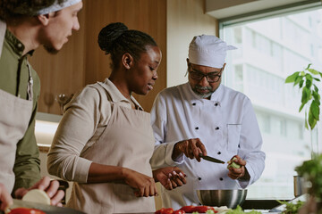 Low angle shot of professional chef showing peeling skills while interns watching him