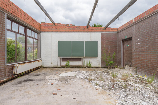 Abandoned classroom in a public accessible with stone debris on floor, and no more roof, view of cloudy sky