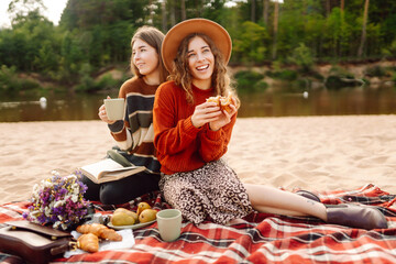 Friendly picnic on the beach. Two girlfriends enjoy a picnic by the river on a sunny day.  Concept of relaxation, nature, travel.