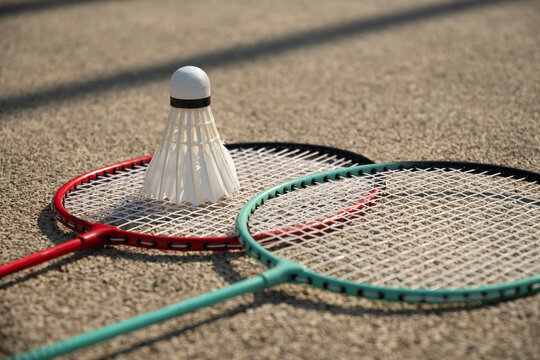 White badminton shuttlecock and badminton rackets on floor sport badminton court in sunny shadow. Outdoors. Close up.