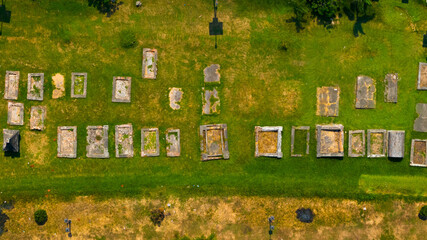 Aerial view of a serene cemetery with a patchwork of tombstones casting shadows over the lush grass, evoking a sense of peaceful finality